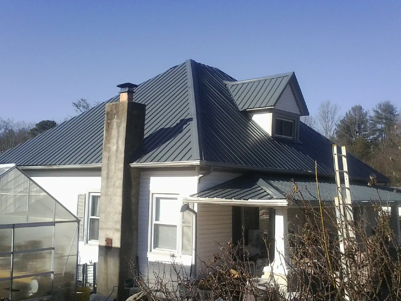 Dark blue standing seam metal roof on a white farmhouse with dormer — Slate & Tile Roof Repair by Roofing Brothers in East Hampton