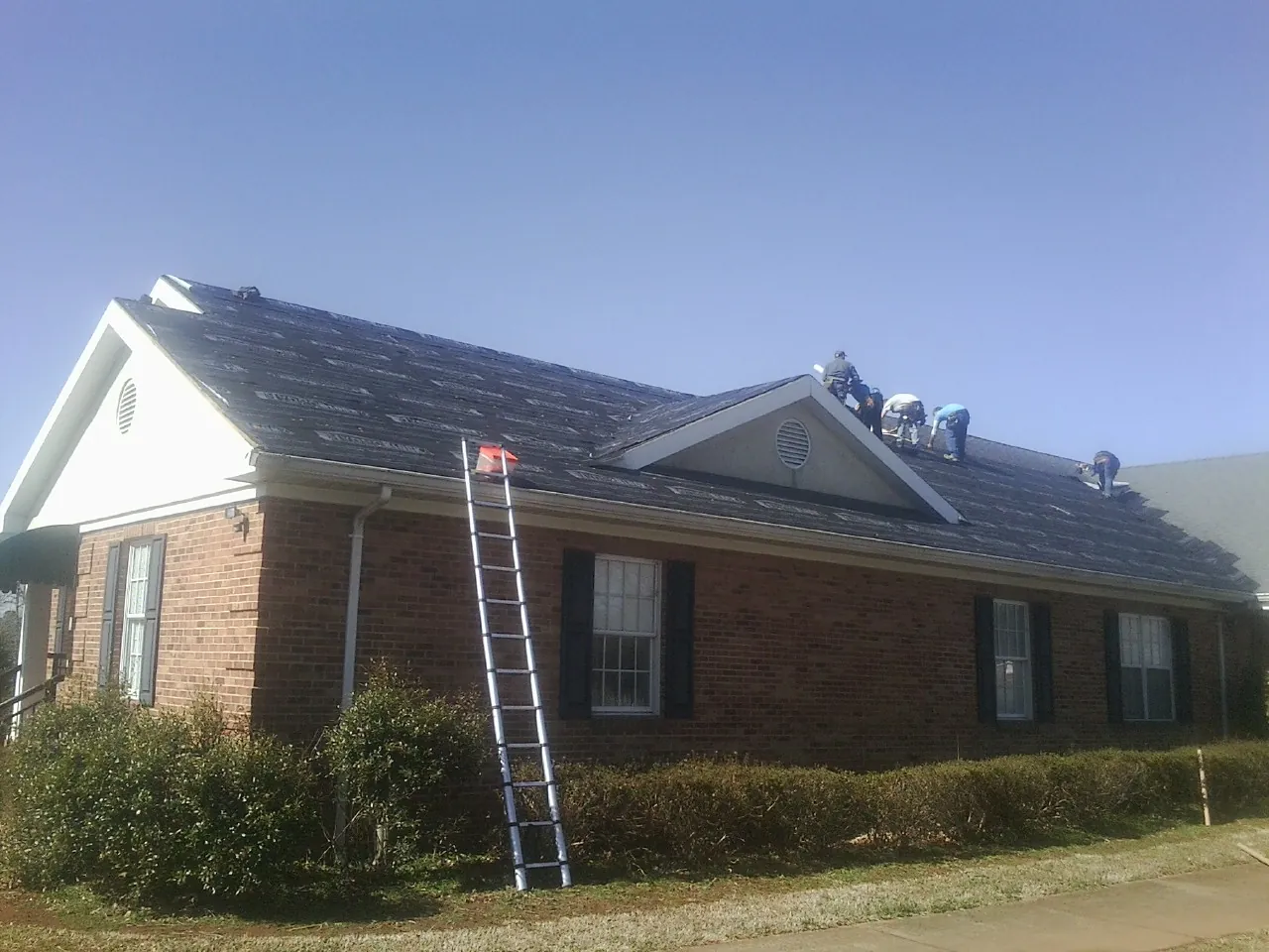 Crew tearing shingles off a brick ranch roof with a ladder set — Metal Roof Repair work by our crew in East Hampton