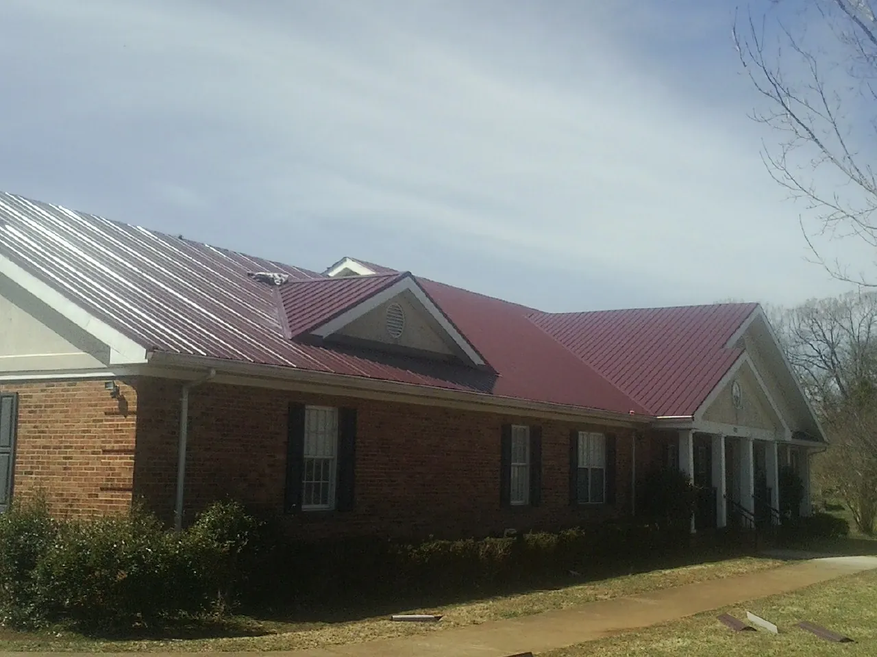 Red metal roof with gabled entries on a long brick building, from a Hail Damage Roof Repair job in East Hampton