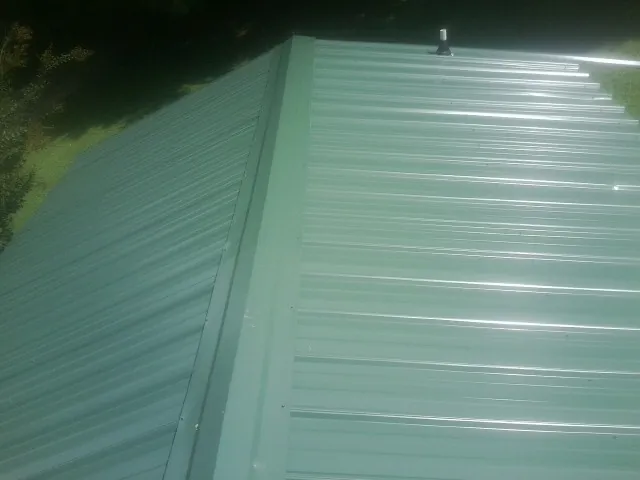 New green metal panels meeting at the ridge of a roof — Flat Roof Repair work by our crew in East Hampton