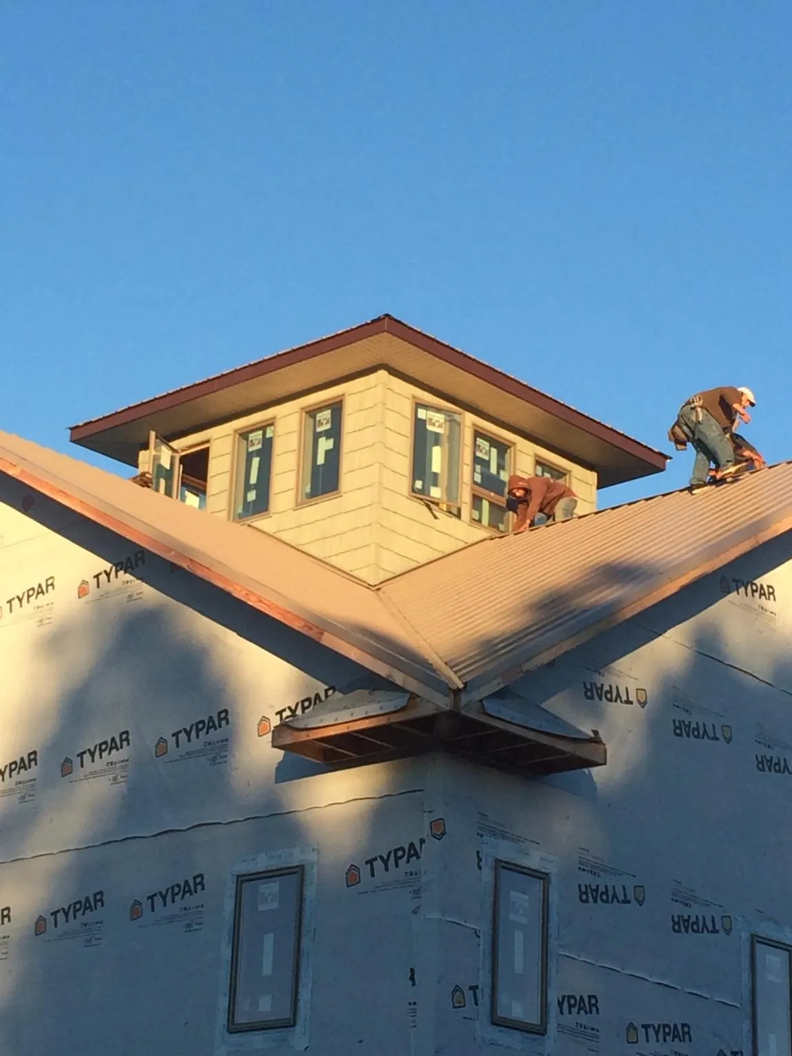 Roofers working around a rooftop cupola on a new metal roof at sunset in East Hampton